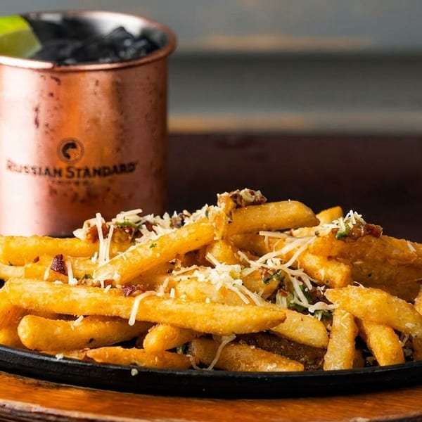 Loaded fries with cheese and herbs on a black plate, next to a copper mug with a lime.