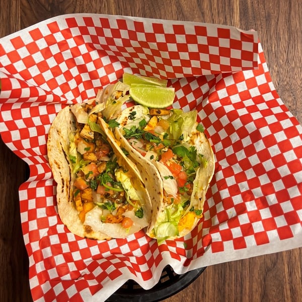 Two chicken tacos with lettuce, salsa, and lime wedges in a red and white checkered basket.