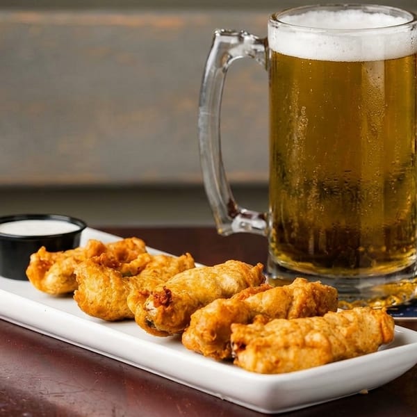 A mug of golden beer with foam next to a plate of fried appetizers and a small cup of dip.