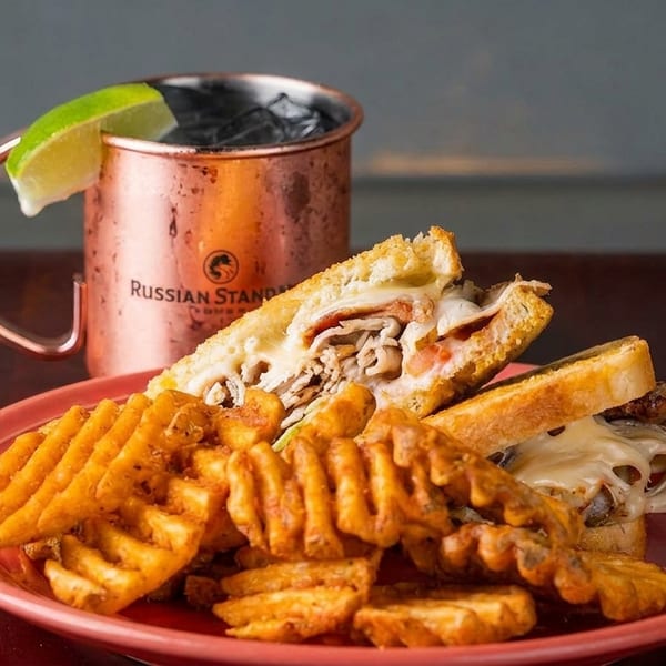 A grilled sandwich with waffle fries on a red plate, next to a copper mug with a lime.