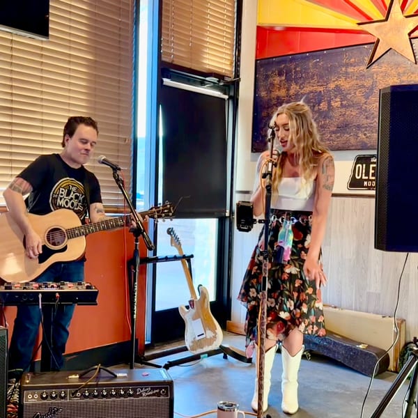A man plays acoustic guitar and a woman sings into a microphone at a restaurant.
