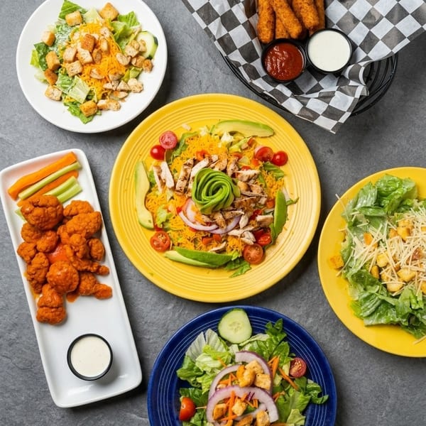 An overhead view of various salads, buffalo cauliflower, and mozzarella sticks with dipping sauces.