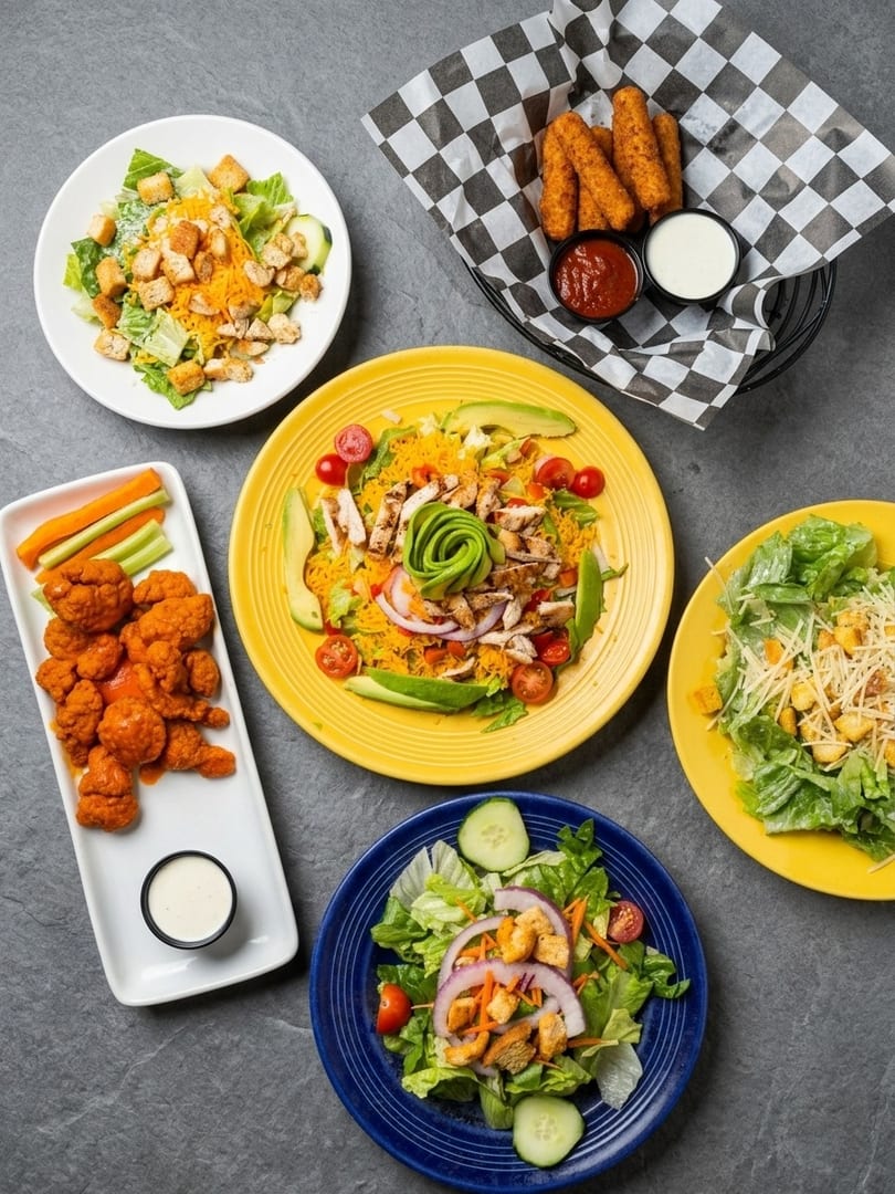 An overhead view of various salads, buffalo cauliflower, and mozzarella sticks with dipping sauces.
